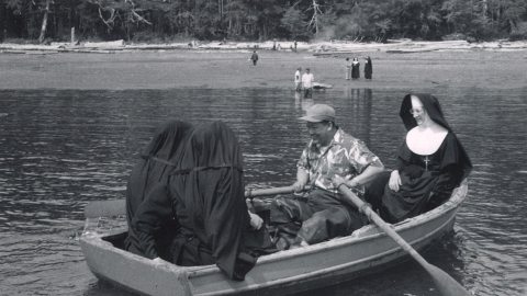 Nuns ride in a boat near the shore while another person rows.