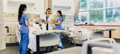 Three care providers stand around a bed in a medical center and have a discussion