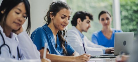 Several healthcare providers sit at a table with writing utensils and computers