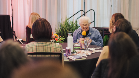 Sister Kathleen Pruitt sits at a table and smiles with other Women of Peace attendees