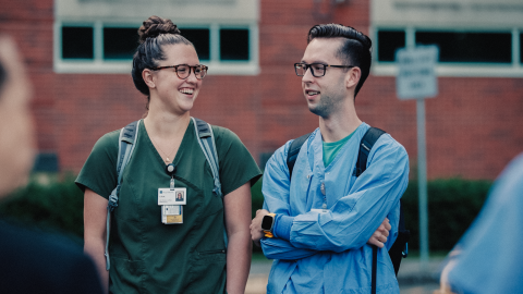 Two nurses outside of a medical center, talking and smiling