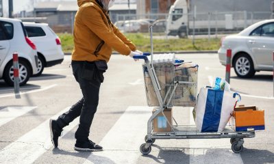 Person wearing a mask and gloves pushes a full grocery cart