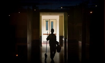 Worker holding a mop walks down a dark hallway