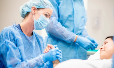 A nurse wearing surgical scrubs holds the hand of a pregnant woman in the OR