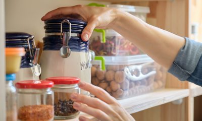 Hands of a woman reaches for a jar in a pantry shelf of dry foods