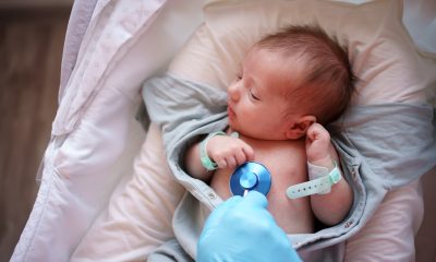 A gloved hand of a doctor holds a stethoscope on the chest of a newborn. 