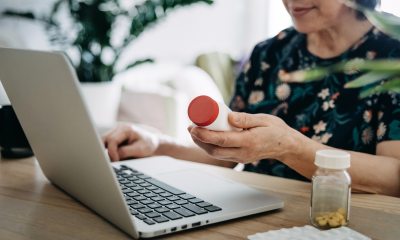 Woman checks medicine bottle as she works on laptop