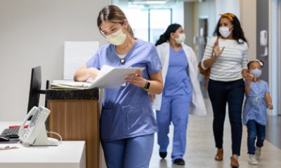 One woman provider reviews chart as another provider walks with two patients in clinic hallway.