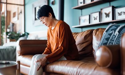Woman sitting on a brown couch rubs her knee