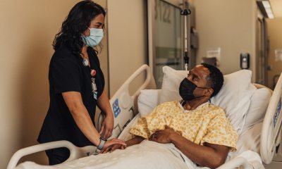 A PeaceHealth nurse stands bedside next to a patient lying in a hospital bed.