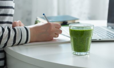 Woman working on computer with green drink next to her.