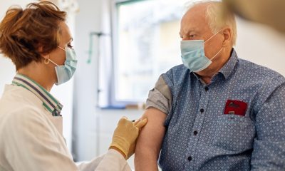 Woman healthcare provider gives immunization in arm of grey-haired man