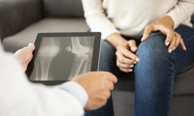 Closeup of doctor's hands holding X-ray and woman pointing to knee