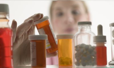 Close-up of bottles of medications in medicine cabinet with blurry image of woman in background