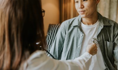 Transgender man meeting with  female doctor who is using a stethoscope on the patient's chest area.
