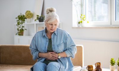 white-haired woman holds hands over stomach as in pain