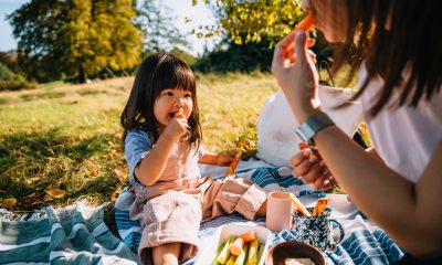 young girl and mom eat picnic on a blanket outdoors