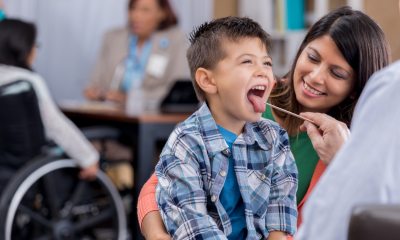 A young boy holds his tongue out as a provider checks his temperature