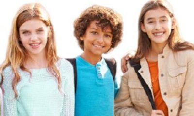 A group of five kids stand shoulder to shoulder smiling