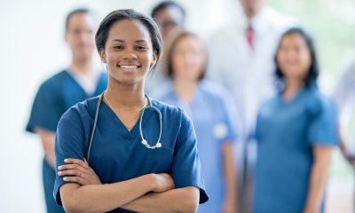 A smiling nurse stands in front of a group of other nurses, blurred in the background