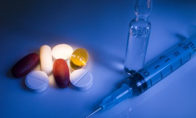 Dark image of a syringe and glass tube on the right with various colored pills highlighted to the left