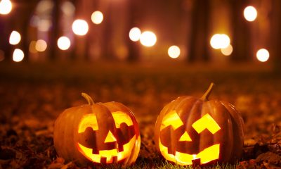 A pair of illuminated jack o' lanterns site on leafy grass at night