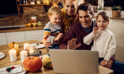 A family in their kitchen in front of a laptop, virtually meeting with others.