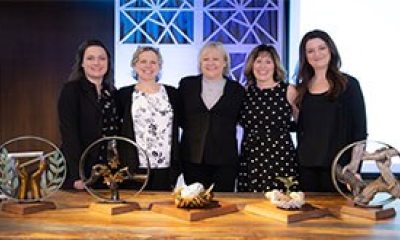 A group of five smiling women standing at a table with awards