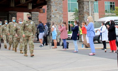 A group of masked PeaceHealth employees claps for masked National Guard members as they march out of the medical center