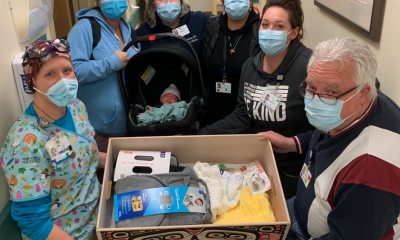 A group of masked healthcare providers escorting a newborn and all of the necessary supplies as they leave the hospital/