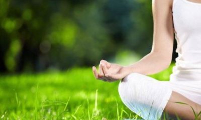 A woman in white performs yoga in a park-like setting.