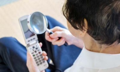 woman uses magnifying glass to read screen of mobile phone
