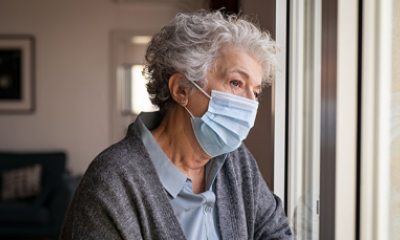 Lonely woman wearing a mask looks out window