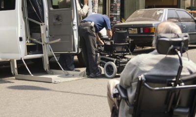 A man in a motorized wheelchair rolls up to another person adjusting a power wheelchair next to van