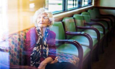 An older lady in purple shirt and scarf looks out a window from her seat