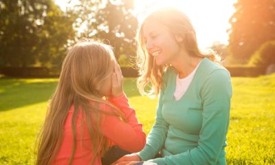 Mother and daughter playing peek-a-boo while sitting in a park, with sublight in the background