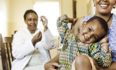 A child smiles in the foreground, with a health care provider in the background