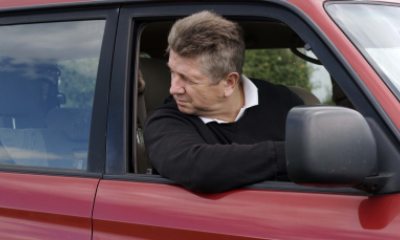 A man drives a car and looks backwards out the window