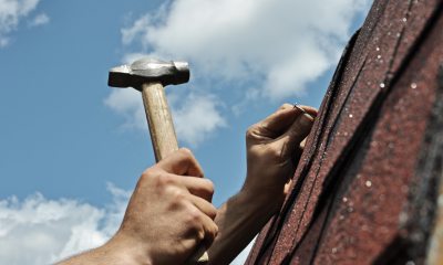 A person hammers nails into a shingle roof