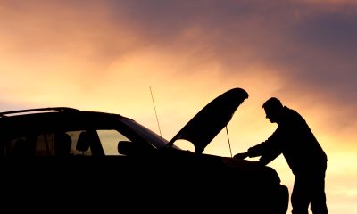Silhouette of a man and car with the hood up, against a sunset of purple and pink hued sky