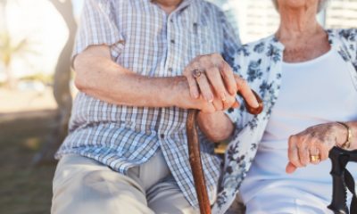 Elderly couple holding hands, a cane and other walking devices