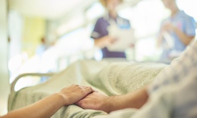 Close-up of a person holding a patient's hand with healthcare providers blurred in the background