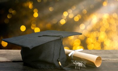 Graduation cap and diploma resting on a table in front of golden light