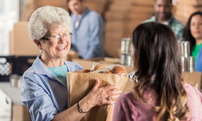 An older woman with a bag of groceries smiles at a person with their back to the camera in the foregorund