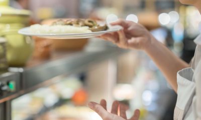 A person collects a plate of food in the cafeteria lunch line