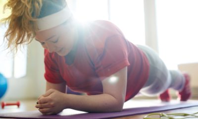 A woman performs a plank exercise on a yoga mat with sunlight beaming in from the background