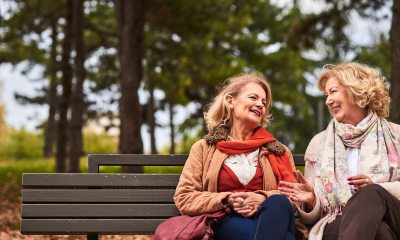 Two women sit on a park bench, smile and chat