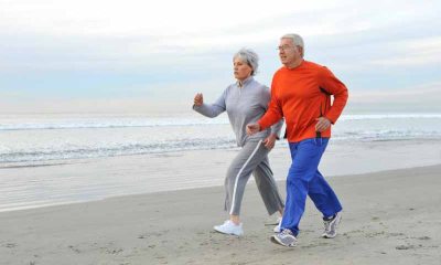An older couple jogs on the beach next to the ocean