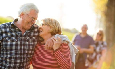 An older couple in the foreground smile and laugh with each other while another couple walks behind