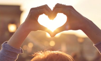 Close-up of hands in a heart shape with the sunlight beaming through